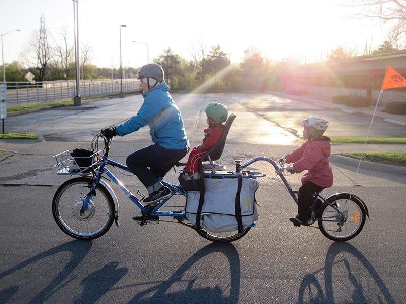 A family cycles to school with bright sun in the background. 